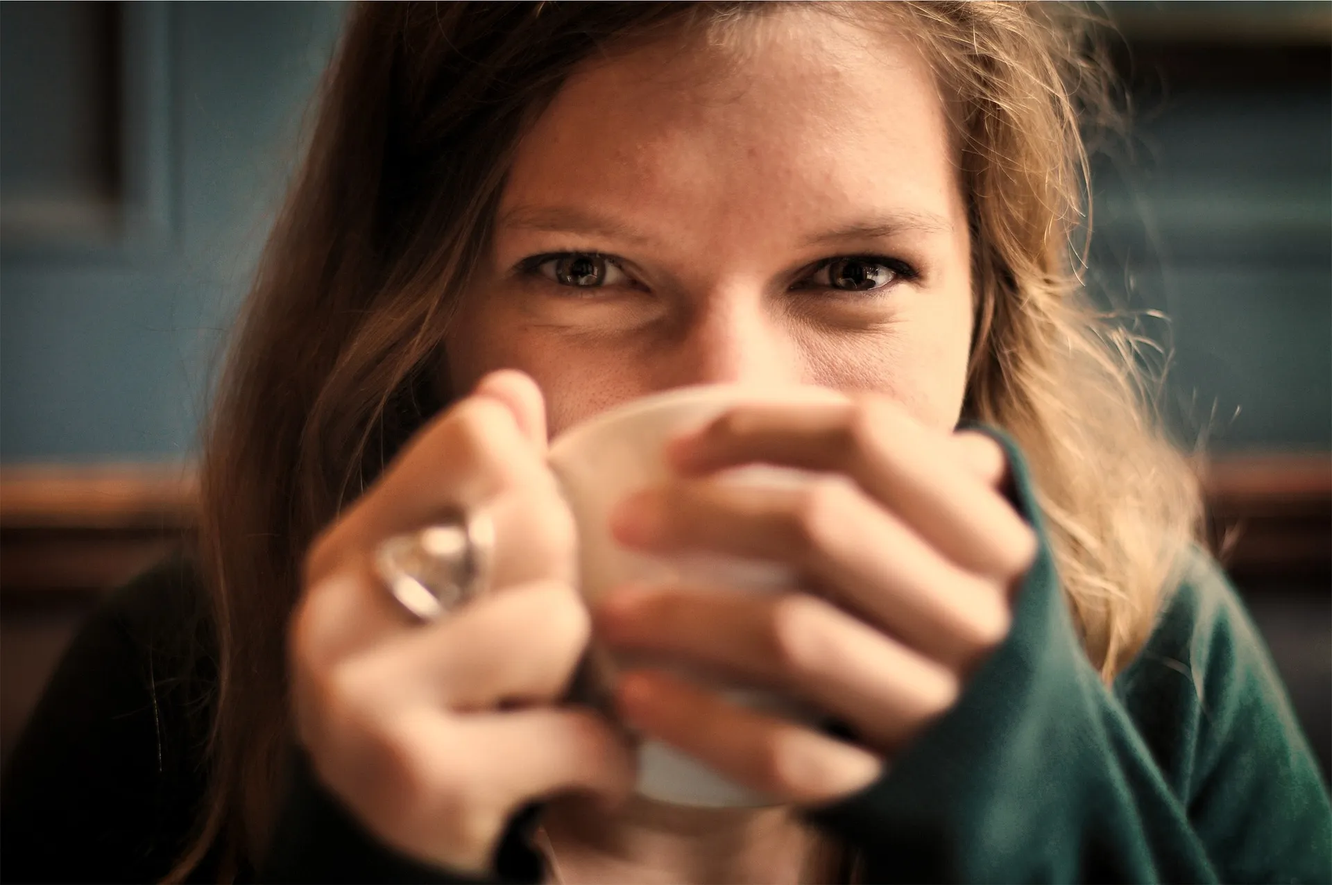 Frau hält eine Tasse mit beiden Händen vor ihr Gesicht und blickt entspannt lächelnd in die Kamera